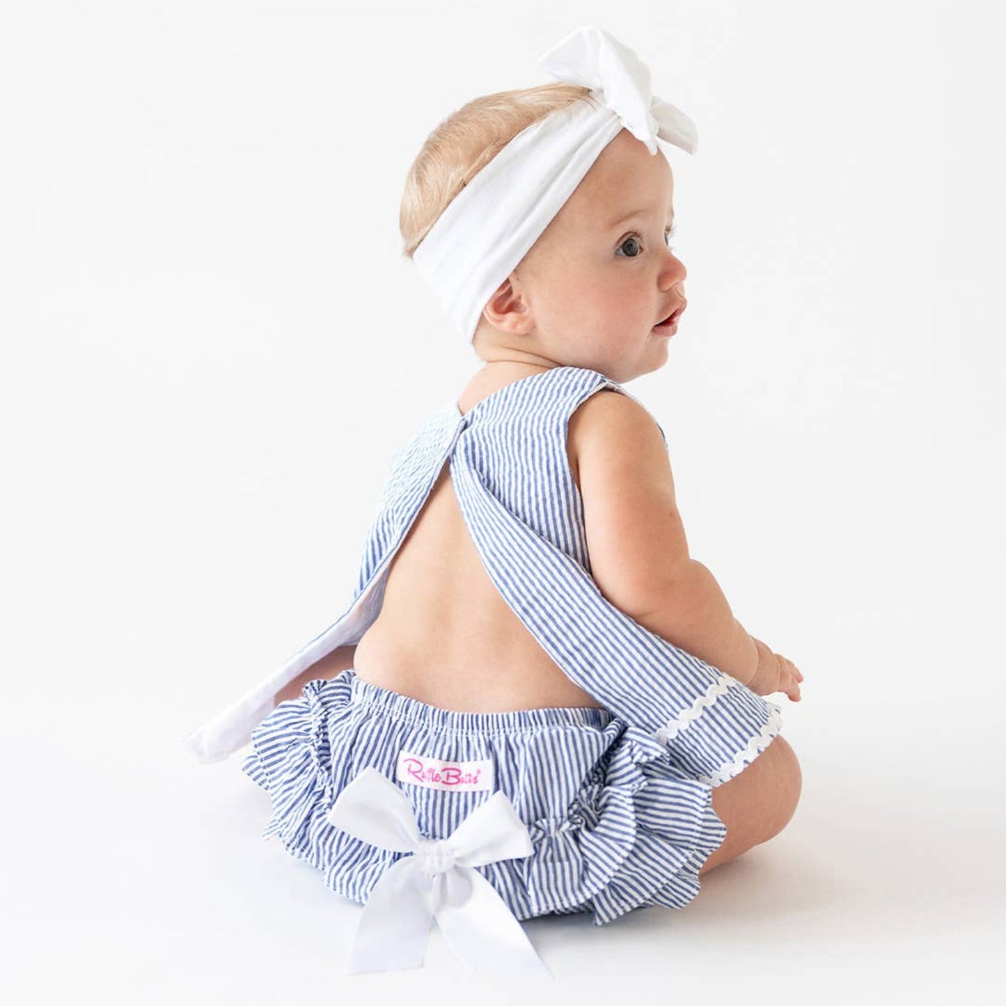 Baby wearing a blue and white striped outfit with a bow on a white background