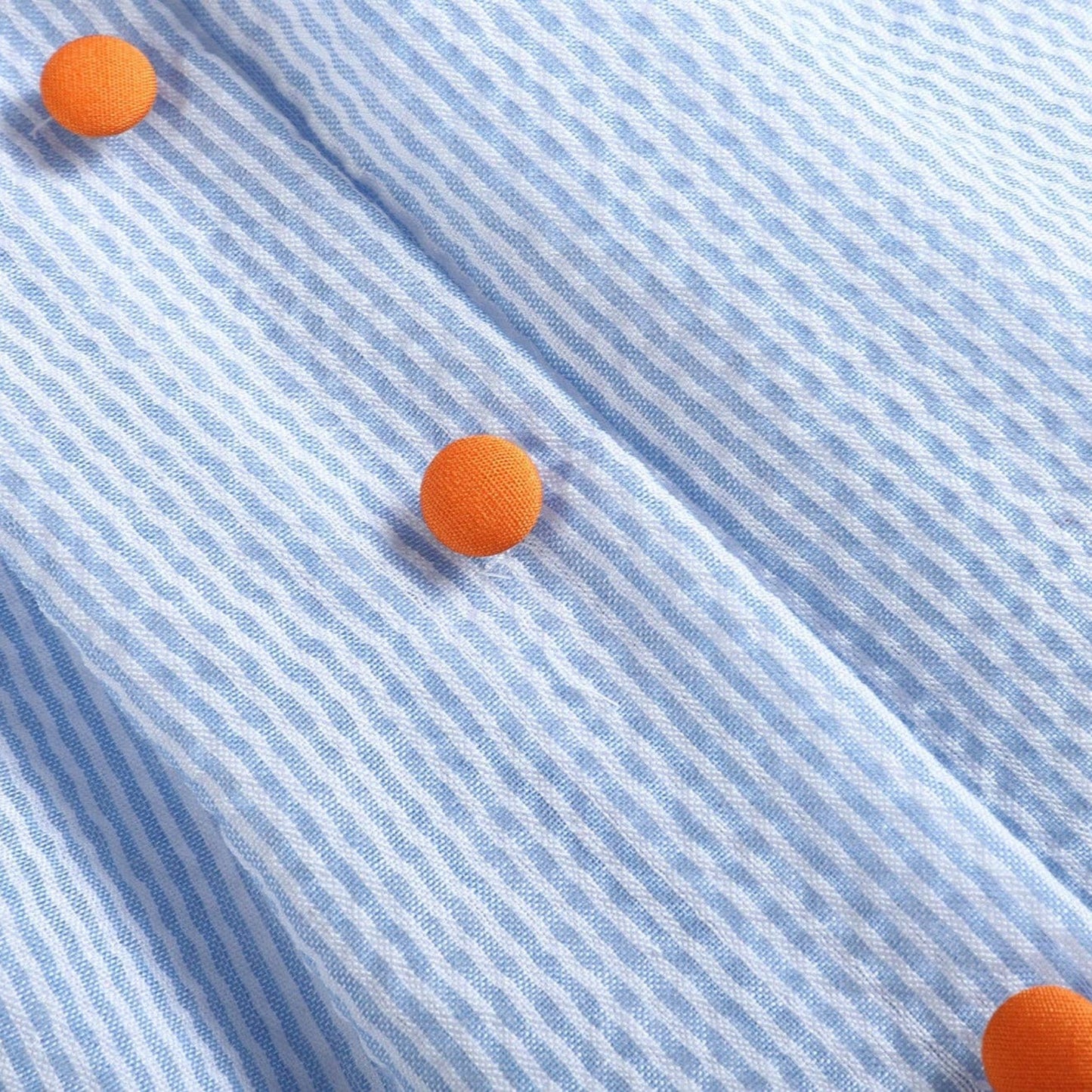 Close-up of a light blue shirt with orange buttons
