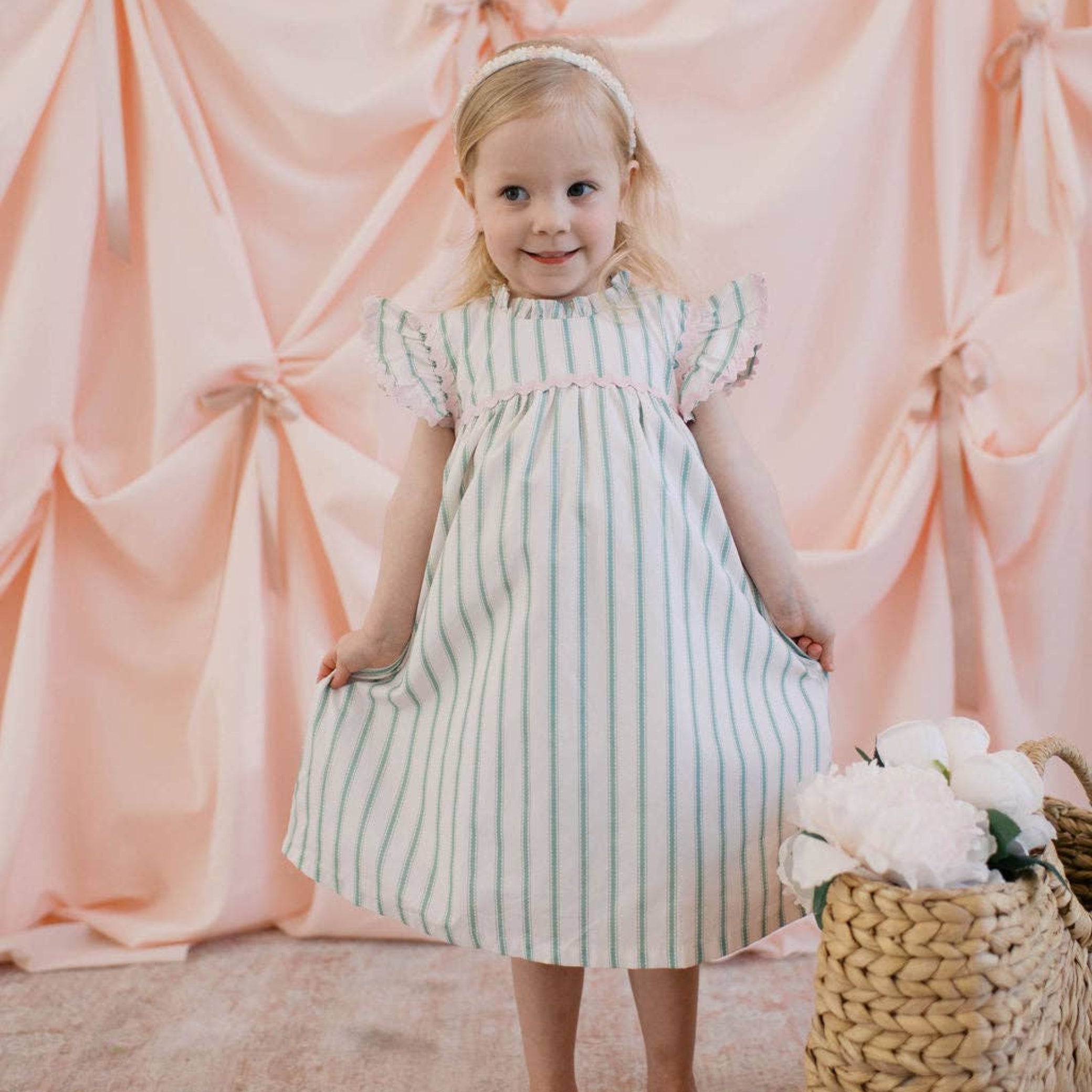 Young girl in a striped dress standing in front of pink draped fabric