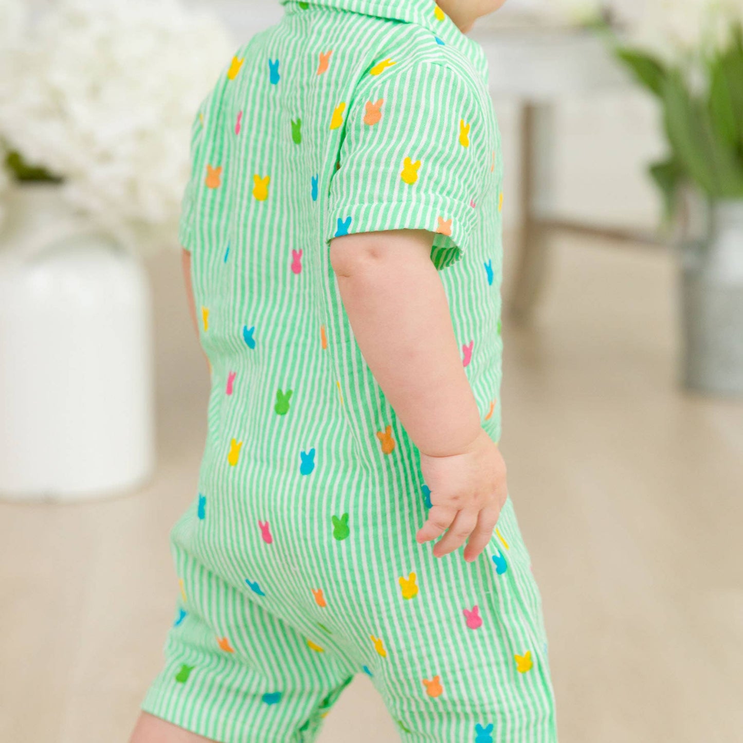Baby wearing a green outfit with colorful patterns in an indoor setting