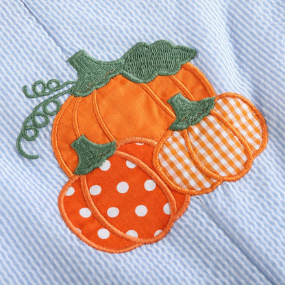 Close-up of an embroidered autumn pumpkin applique on a light blue ribbed fabric, featuring three orange pumpkins with green stems, one with white polka dots and one with orange-and-white gingham check.