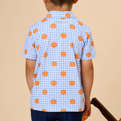 A young boy viewed from behind wearing a light blue and white gingham short-sleeve shirt with an orange pumpkin print, set against a solid beige background.