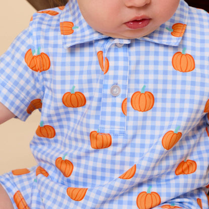 A close-up of a baby wearing a light blue and white gingham short-sleeve polo romper with an orange pumpkin print.