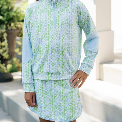 Young girl wearing a light blue and green patterned outfit standing outdoors.