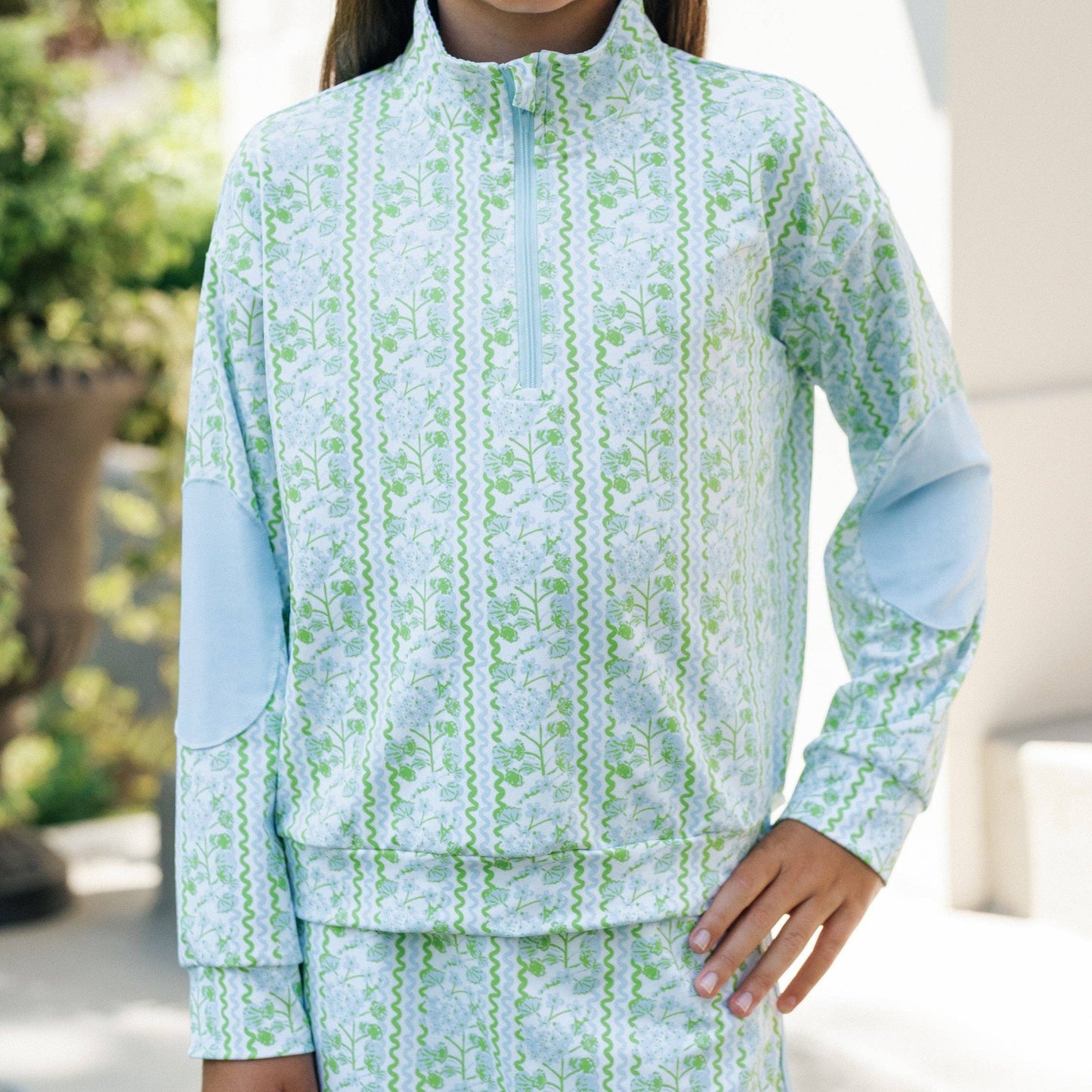 Child wearing a light blue and green patterned outfit outdoors.