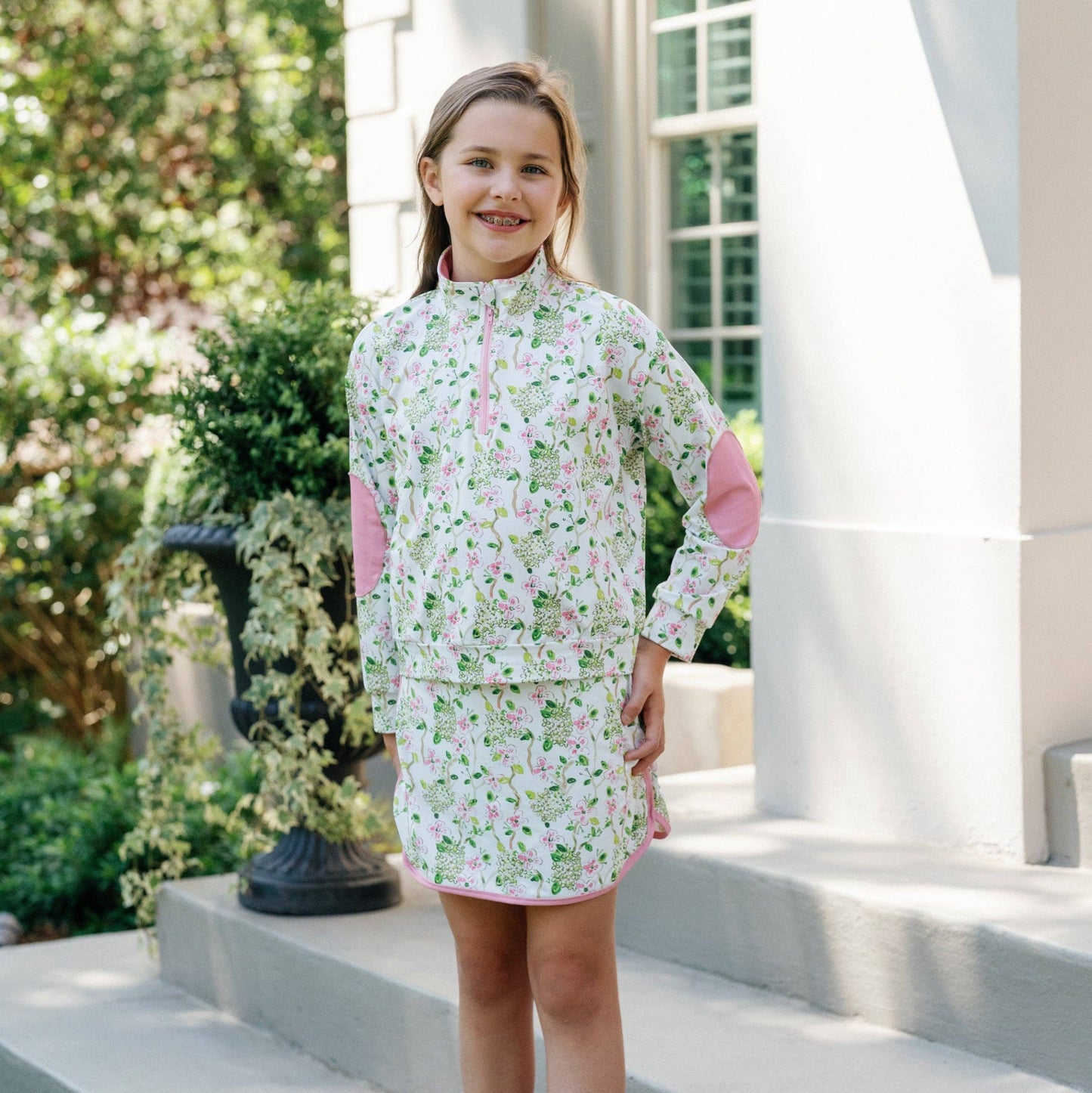 Young girl in a floral skirt and top standing on steps outdoors