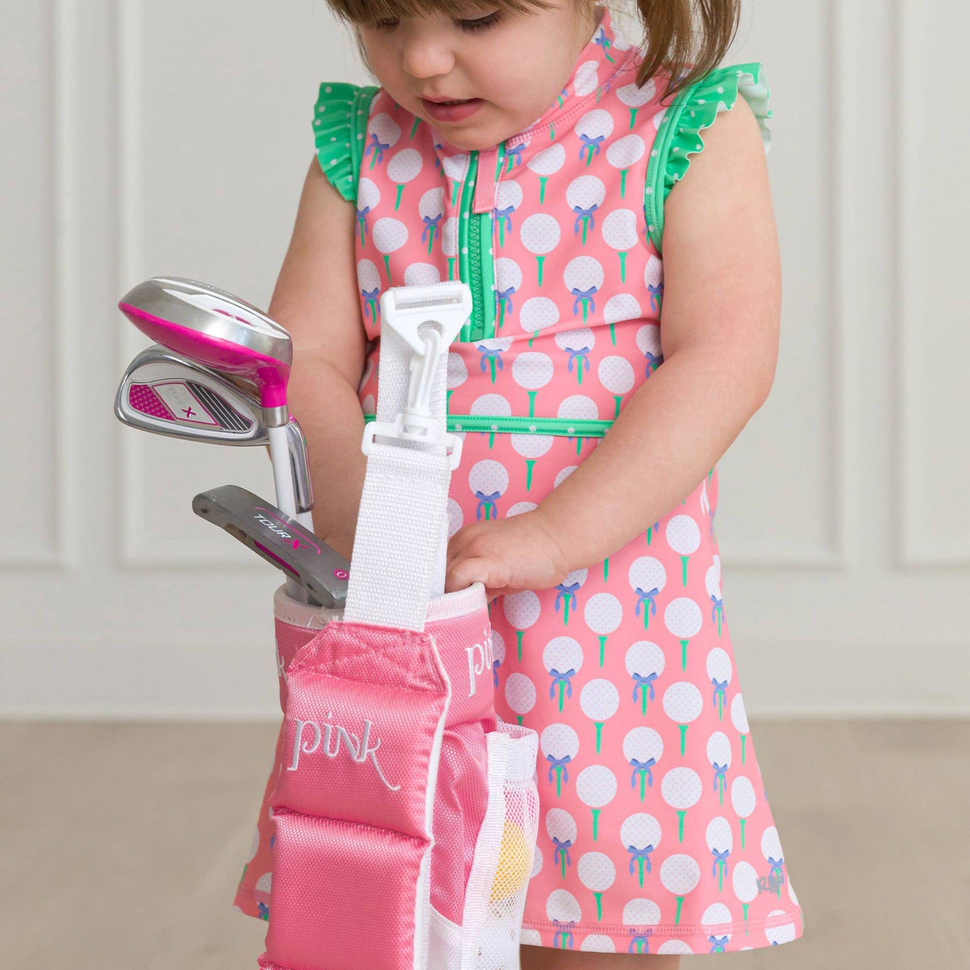 Child in a pink dress with golf clubs and accessories