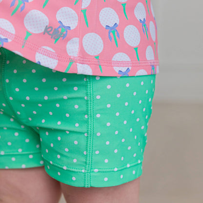 Pink top with dandelion pattern and green shorts with white polka dots on a neutral background