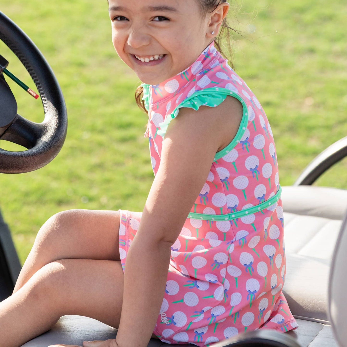 Young girl in a pink polka dot dress with a bow sitting on a golf cart.