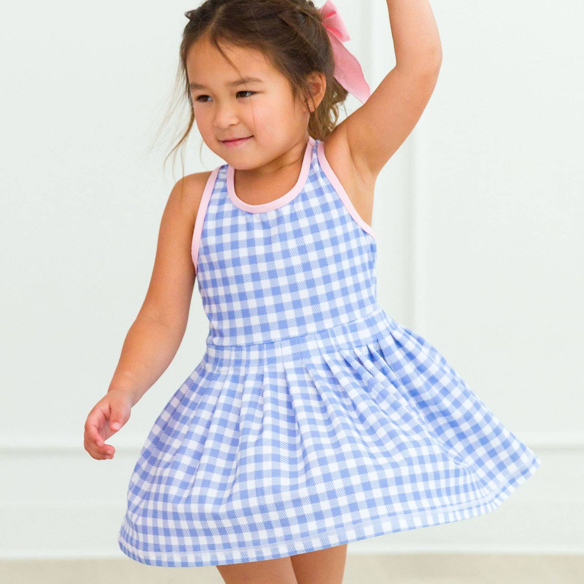 Young girl wearing a blue and white checkered dress against a plain background