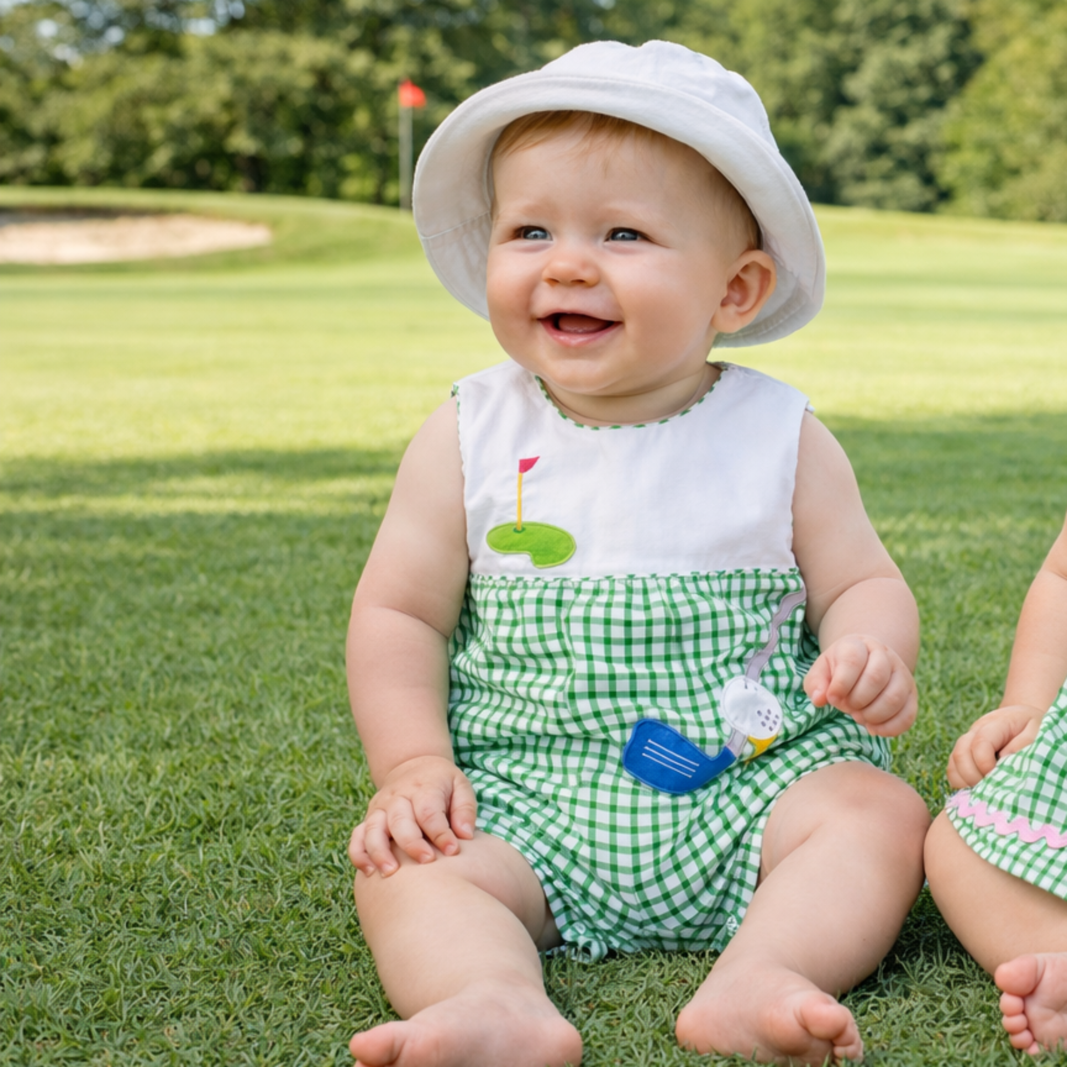 Two children in matching outfits sitting on a golf course.