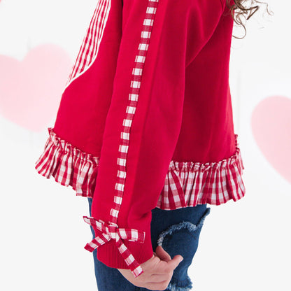 Red dress with checkered details worn by a child against a heart-themed background