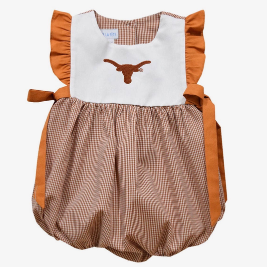 A toddler girl's sleeveless bubble romper dress in a burnt orange and white gingham pattern, featuring a solid white bib-style chest panel with an embroidered orange Texas Longhorns logo, and solid orange-brown ruffle trim and side ties.