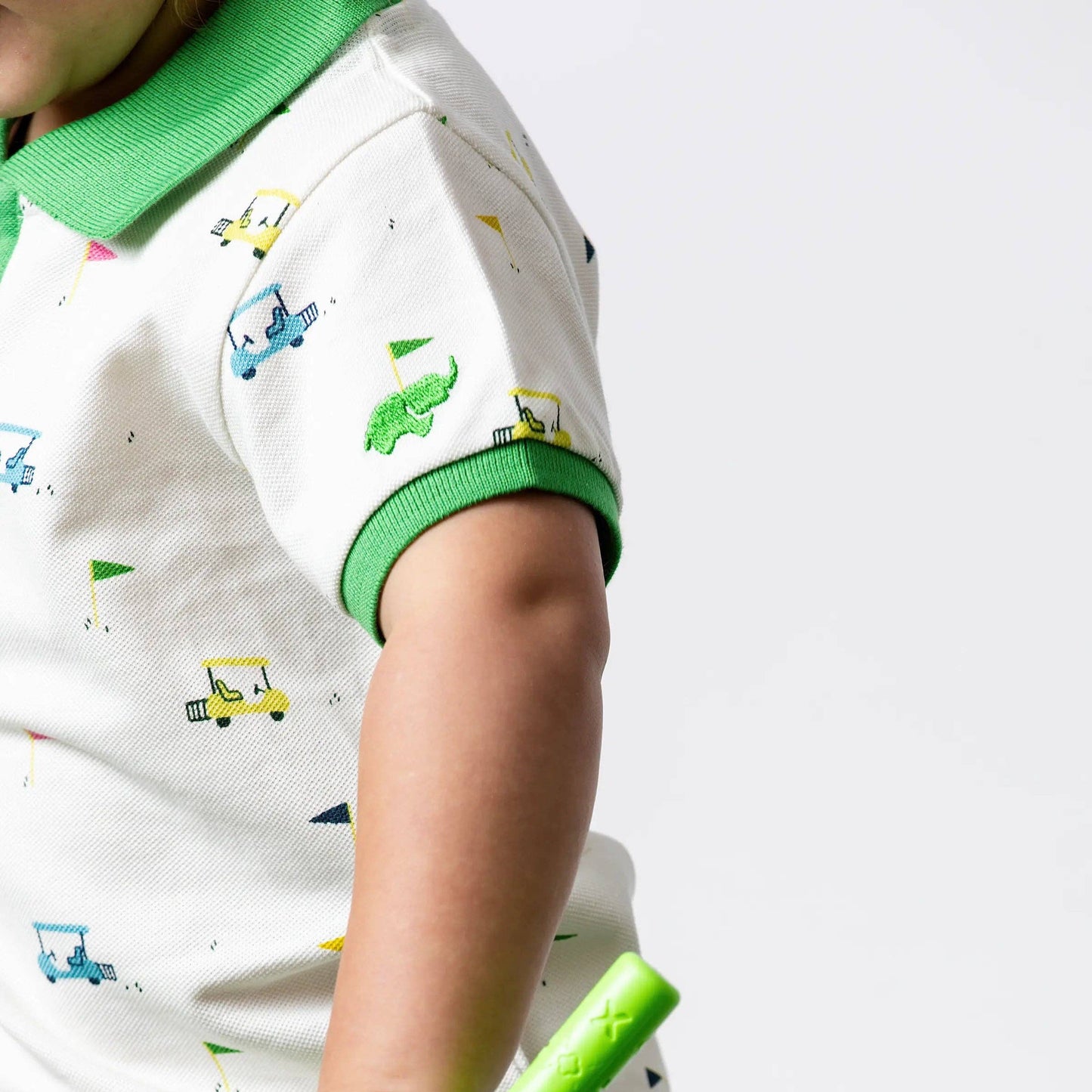 Child wearing a shirt with vehicle prints holding a green toy golf club.