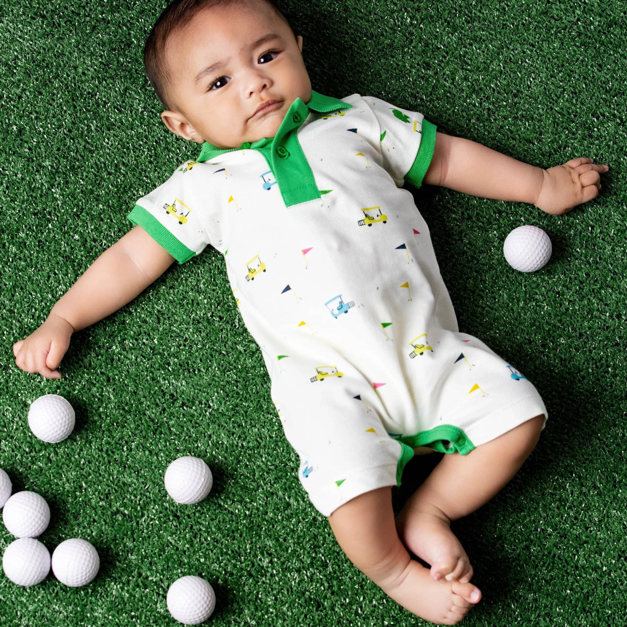 Baby lying on a green surface in romper with golf print with white golf balls around