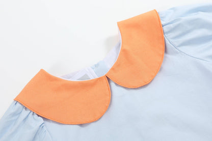 A close-up of a light blue garment with a contrasting orange Peter Pan collar.