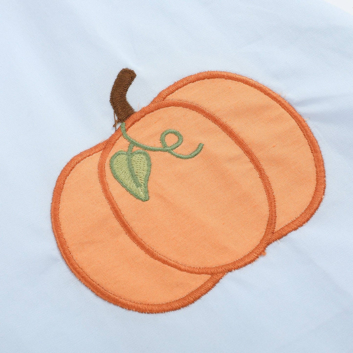 An embroidered orange pumpkin patch with a green leaf and brown stem on a light blue fabric background.