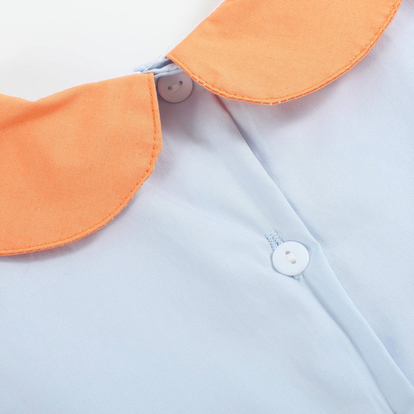 Close-up of a light blue shirt with an orange collar and buttons.