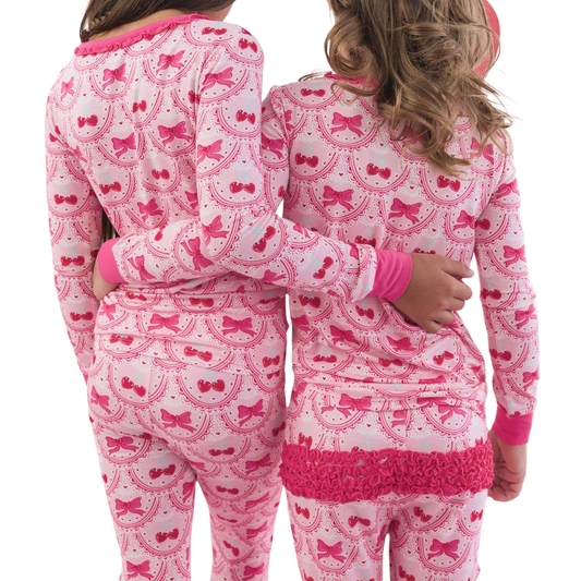 Two children wearing pink and white pajamas with bow patterns on a white background.