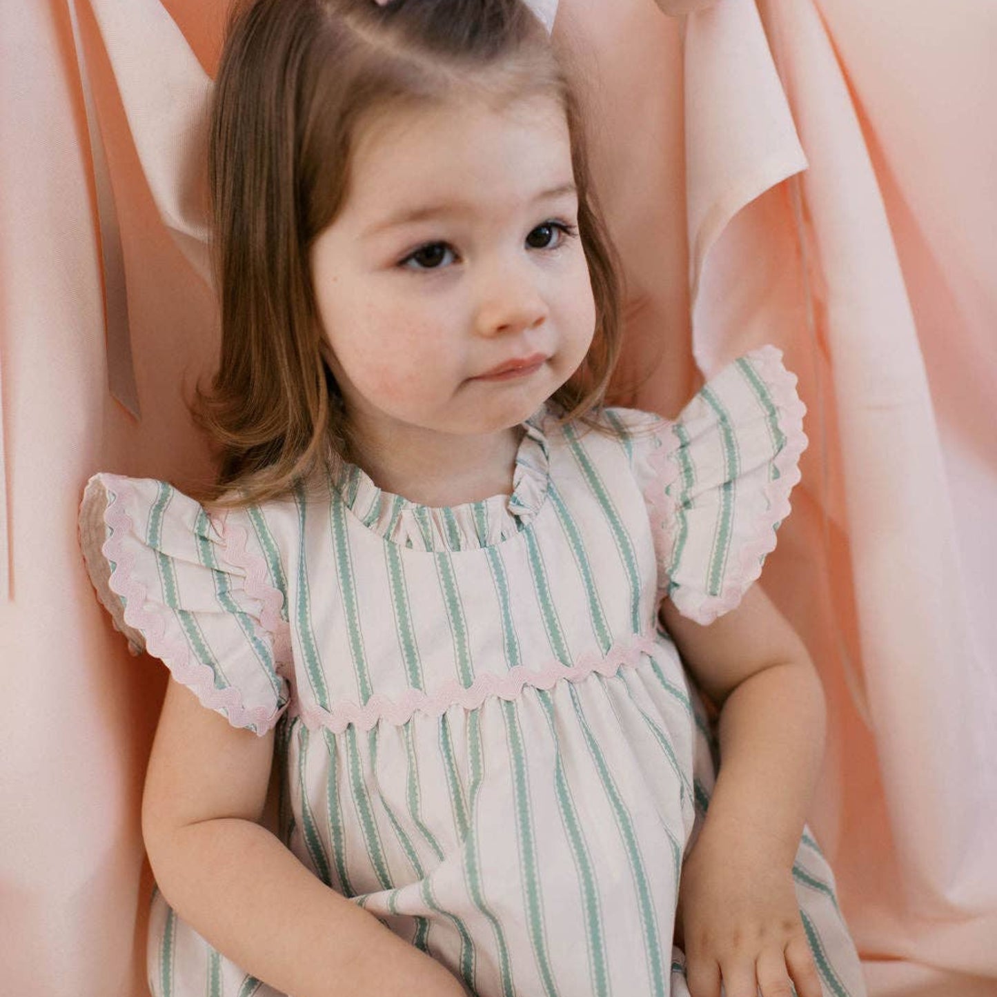 Young girl in a striped dress with ruffled sleeves against a pink background