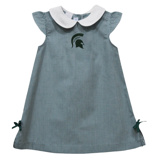 A toddler girl's dress featuring a green and white gingham pattern, a white Peter Pan collar, and a dark green Michigan State Spartans helmet logo on the chest. It has ruffled cap sleeves and small side bows.