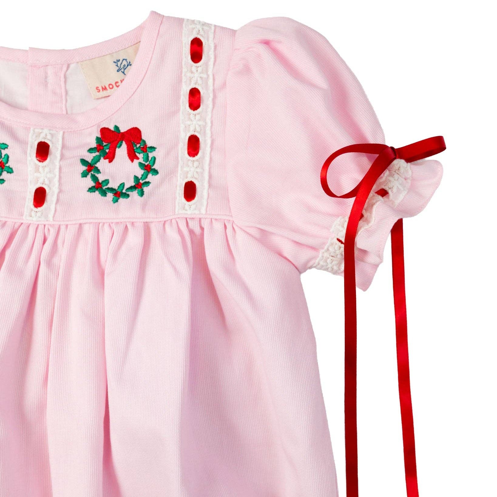 Pink baby dress with red ribbon and Christmas wreath design on a white background