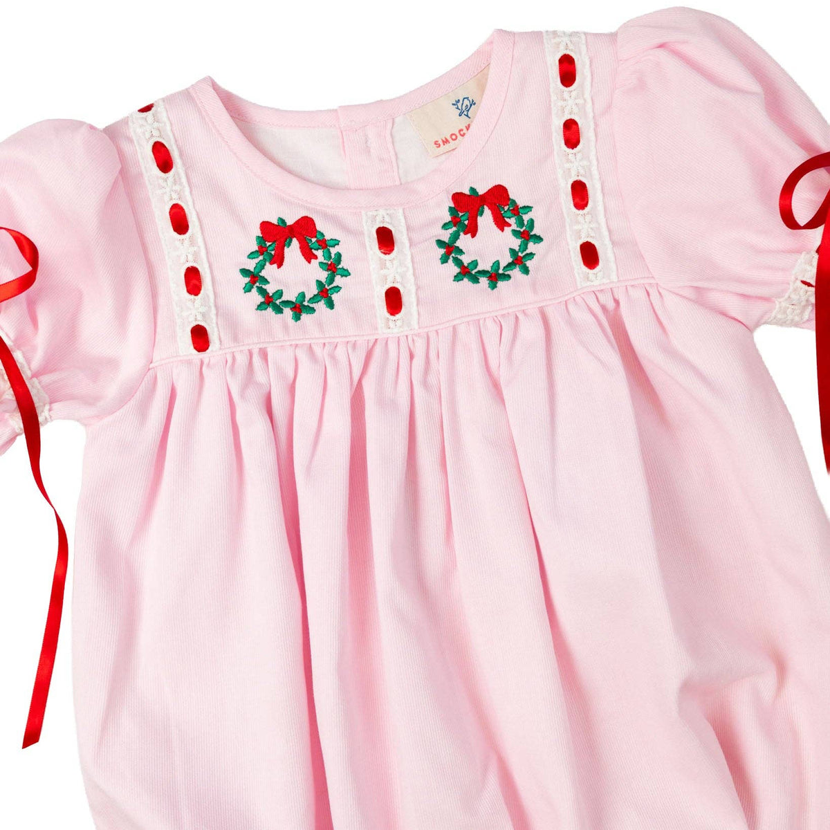 Pink baby dress with Christmas wreath and bow details on a white background