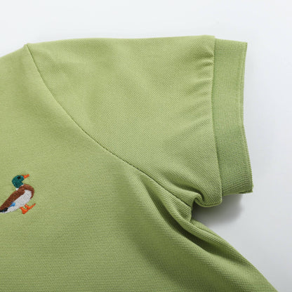 A close-up of a light olive green polo shirt showing the collar, sleeve cuff, and a small embroidered mallard duck logo on the chest, set against a plain white background.