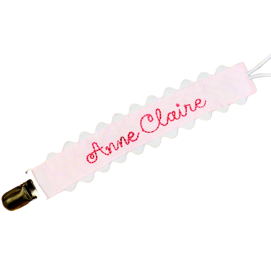 Pink paci clip with scalloped edges on white background