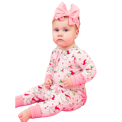 Baby in a pink gingham Christmas pajamas with a bow on a white background