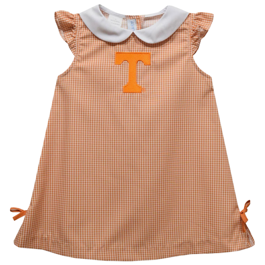 A toddler girl's sleeveless dress with a brown and white gingham pattern, featuring a white Peter Pan collar, ruffled cap sleeves, side ties, and a large orange block letter 'T' on the chest.