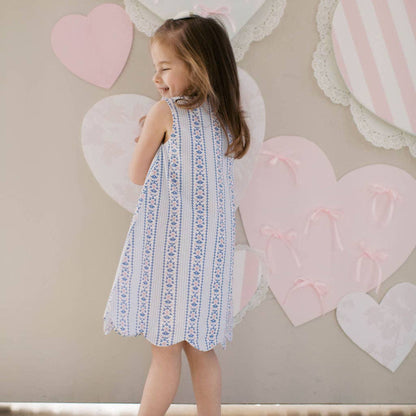 Young girl in a dress standing in front of a wall with heart-shaped decorations.