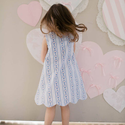 Child in a white dress standing in front of a wall with heart-shaped decorations.